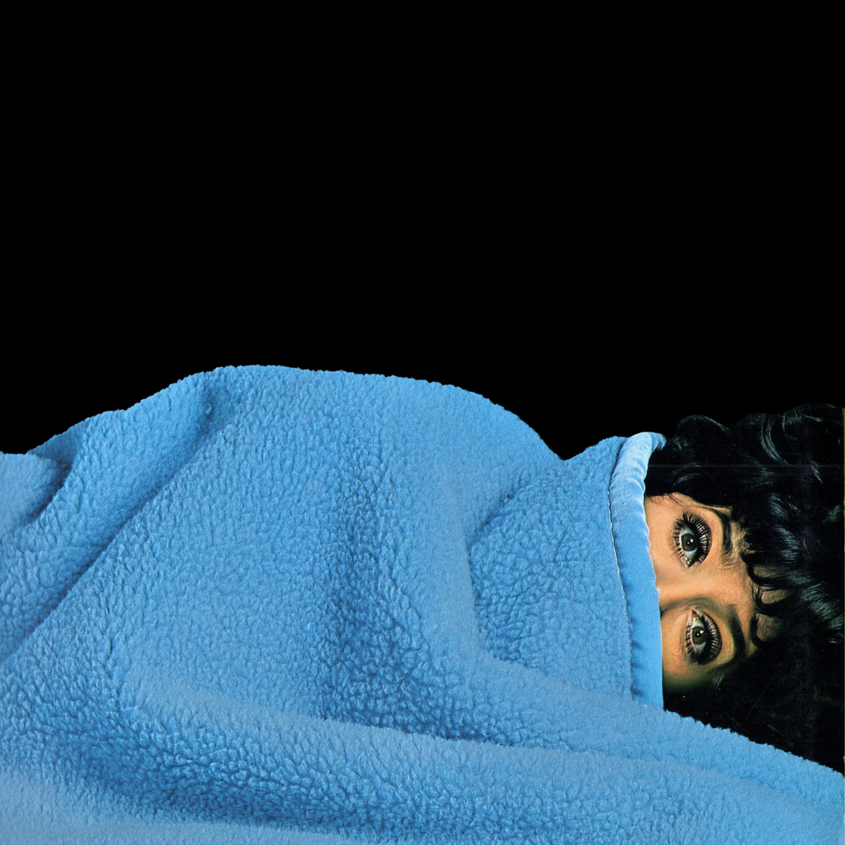 Das Katalog-Cover zeigt eine Frau, die bis zu den Augen unter einer blauen Wohndecke liegt.